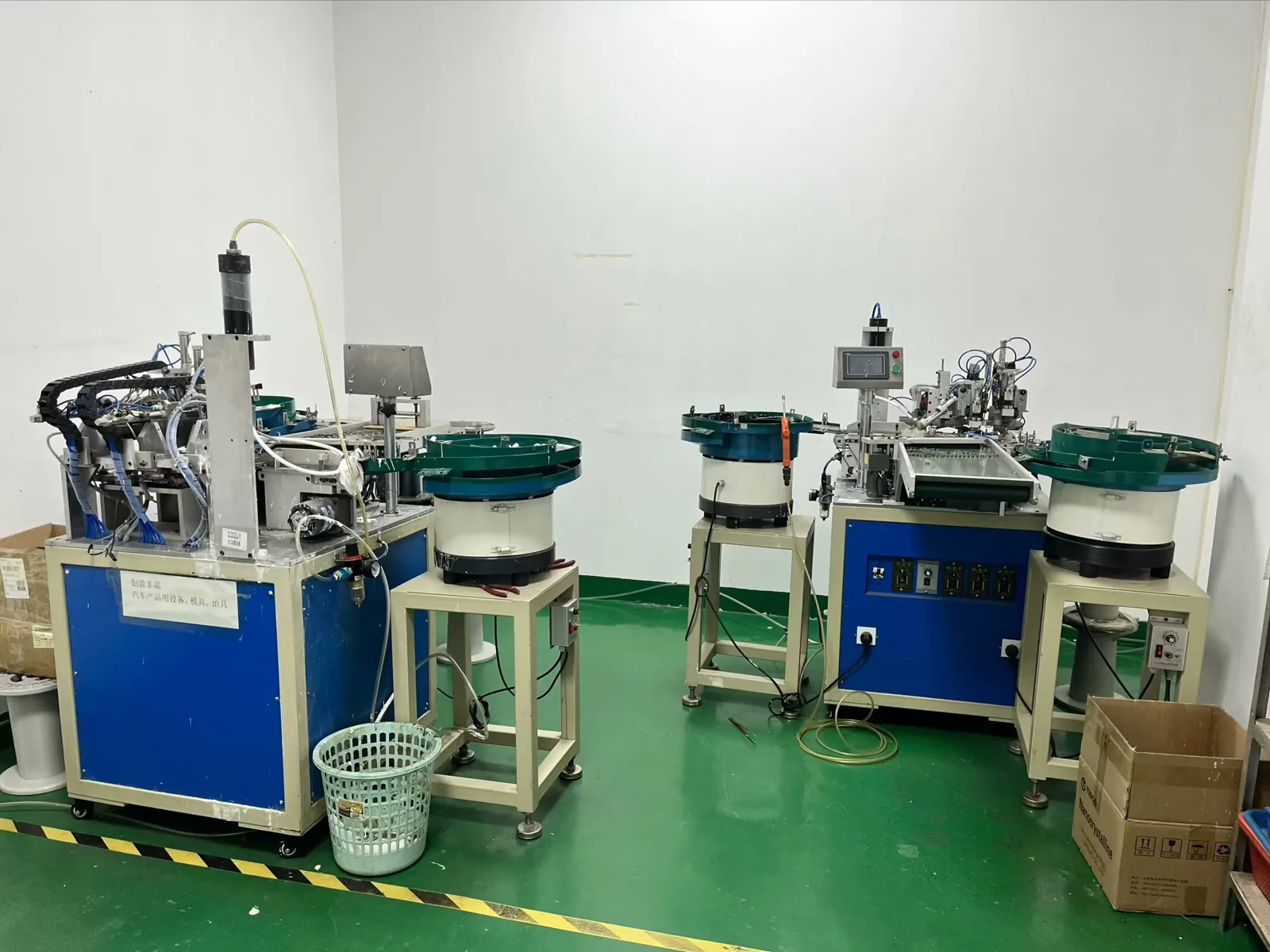 Two automatic production machines with vibratory bowl feeders on a green workshop floor